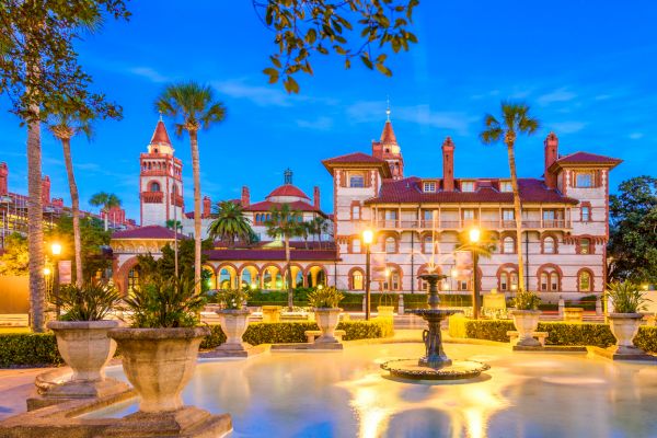 A historic building with palm trees, vibrant lighting, and a fountain in front at twilight.