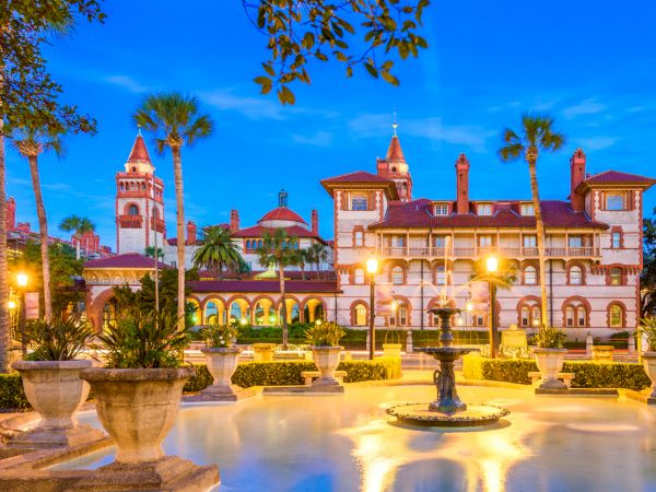 A historic building with palm trees, vibrant lighting, and a fountain in front at twilight.