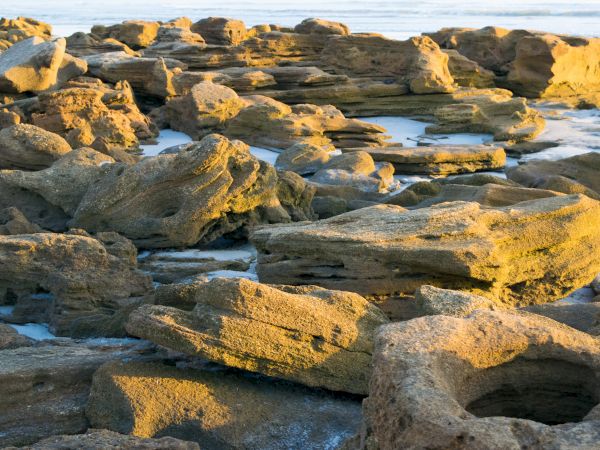 The image shows a rugged, rocky coastal area with large rocks warmed by sunlight near the ocean's edge.