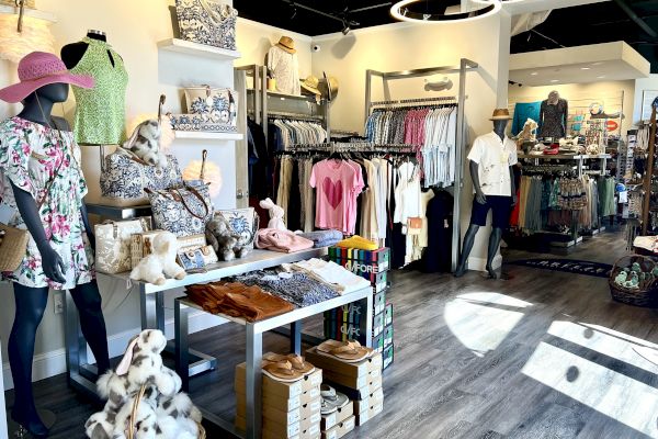 A clothing boutique with mannequins, summer outfits, accessories, and shelves displaying bags and stuffed animals, all in a well-lit interior.