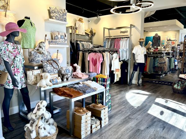 A clothing boutique with mannequins, summer outfits, accessories, and shelves displaying bags and stuffed animals, all in a well-lit interior.