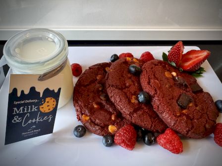 A jar of milk and cookies next to a plate of red cookies with berries on a white surface.