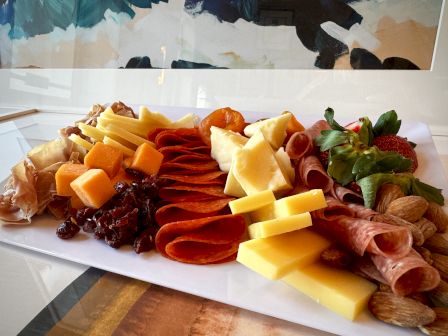 A charcuterie board with assorted cheeses, cured meats, crackers, fruit, and a mint garnish arranged on a rectangular platter.
