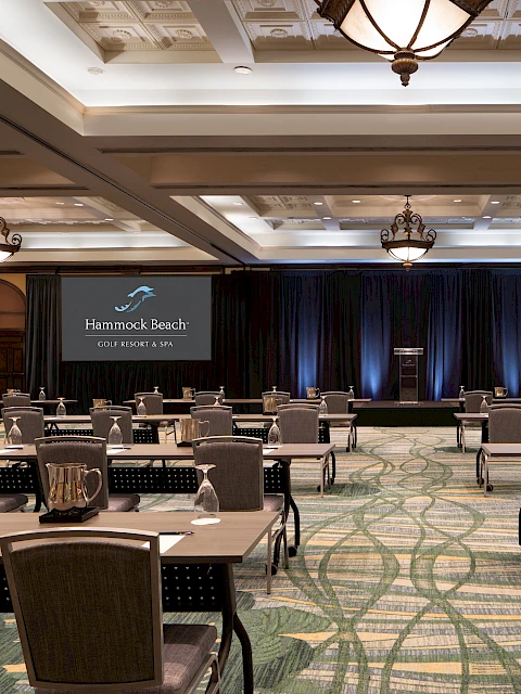 A spacious conference room set up with tables, chairs, and screens displaying "Hammock Beach Golf Resort & Spa", ready for a presentation.