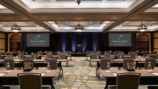 A spacious conference room set up with tables, chairs, and screens displaying "Hammock Beach Golf Resort & Spa", ready for a presentation.