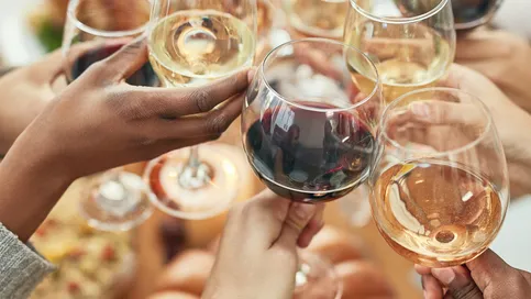 Friends clink wine and champagne glasses at a festive dinner party, smiling and toasting together.