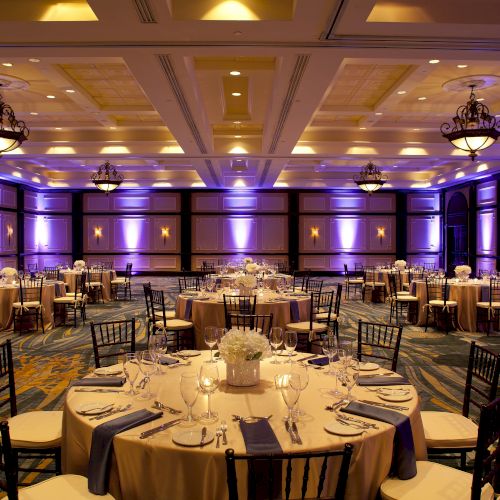 The image shows an elegantly set banquet hall with round tables, chairs, and ambient lighting.