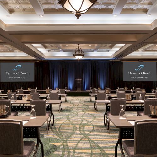 A conference room at Hammock Beach Resort & Spa with tables, chairs, screens, and elegant lighting.