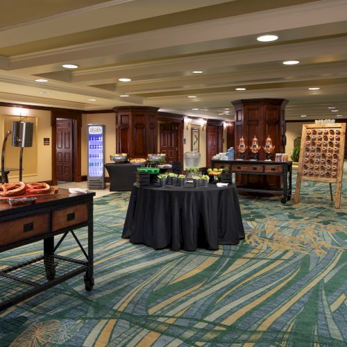 A spacious room with tables set up for a buffet, featuring food, drinks, and a decorated carpet.