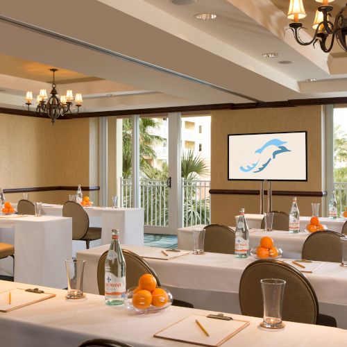 A conference room with tables set with oranges, water bottles, notepads, and pencils. There's a screen showing a dolphin logo.