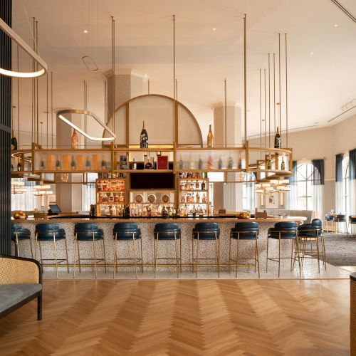 The image shows a stylish bar with modern design, featuring blue stools, a curved counter, and decorative lighting fixtures.