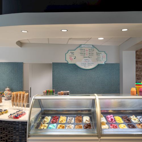 An ice cream shop interior with a display of various gelato flavors, waffle cones, and colorful toppings.