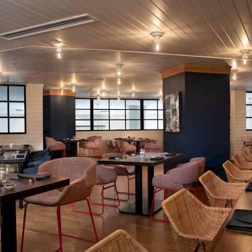 The image shows a modern restaurant interior with wooden tables, cushioned chairs, bar seating, and soft lighting.