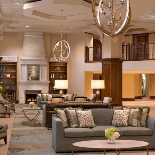 Elegant lobby with a cozy sofa, decorative cushions, a fireplace, plants, and stylish chandeliers creating a warm ambiance.