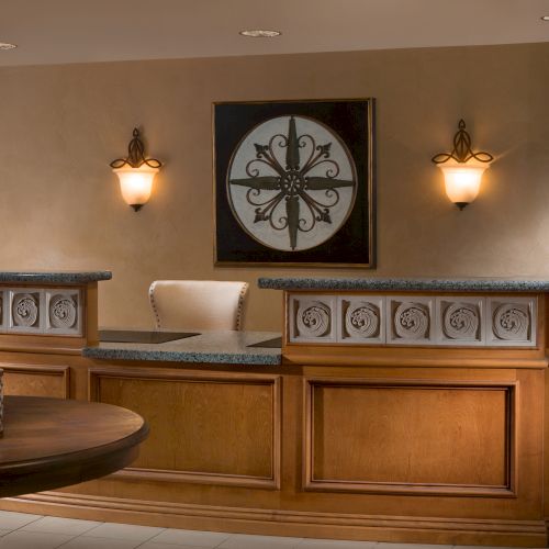 A reception area with a wooden counter, decorative paneling, wall art, lights, a round table with candles, and green bottles.
