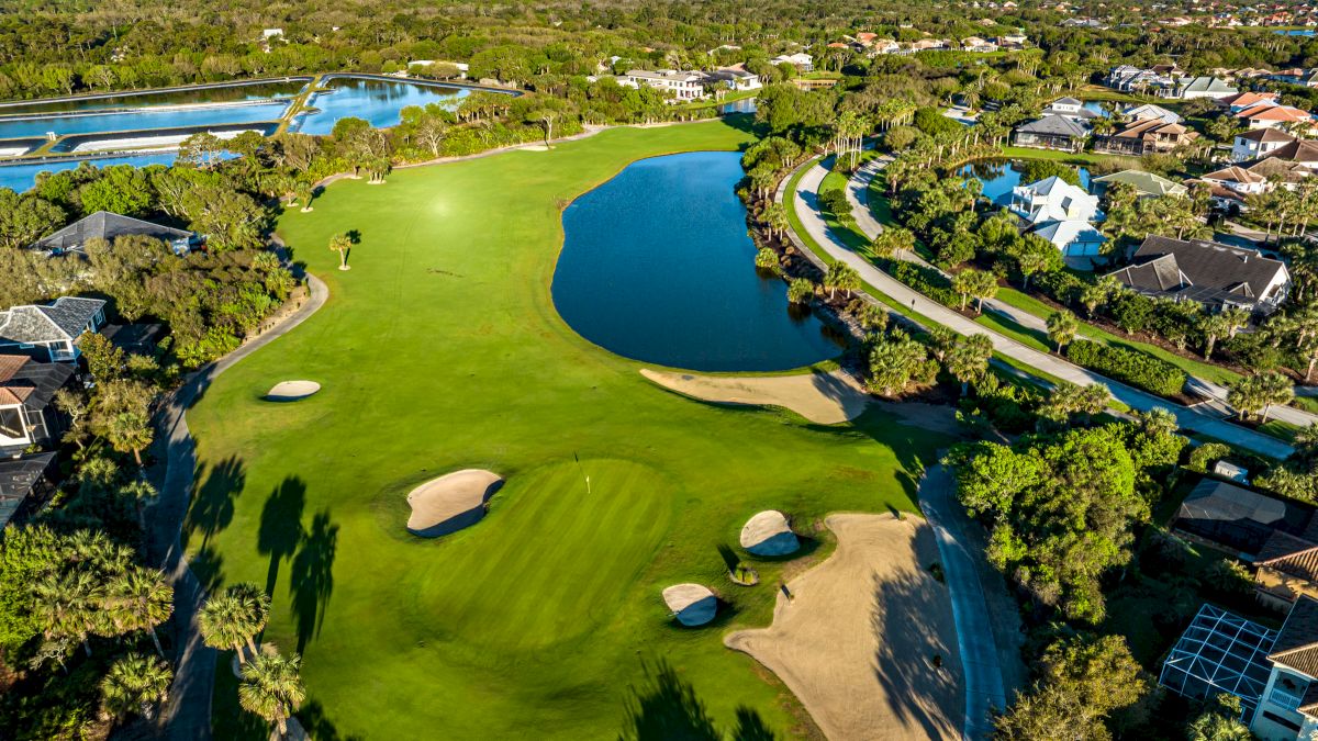 Aerial view of a lush golf course with sand traps, water hazards, and surrounding homes and greenery.