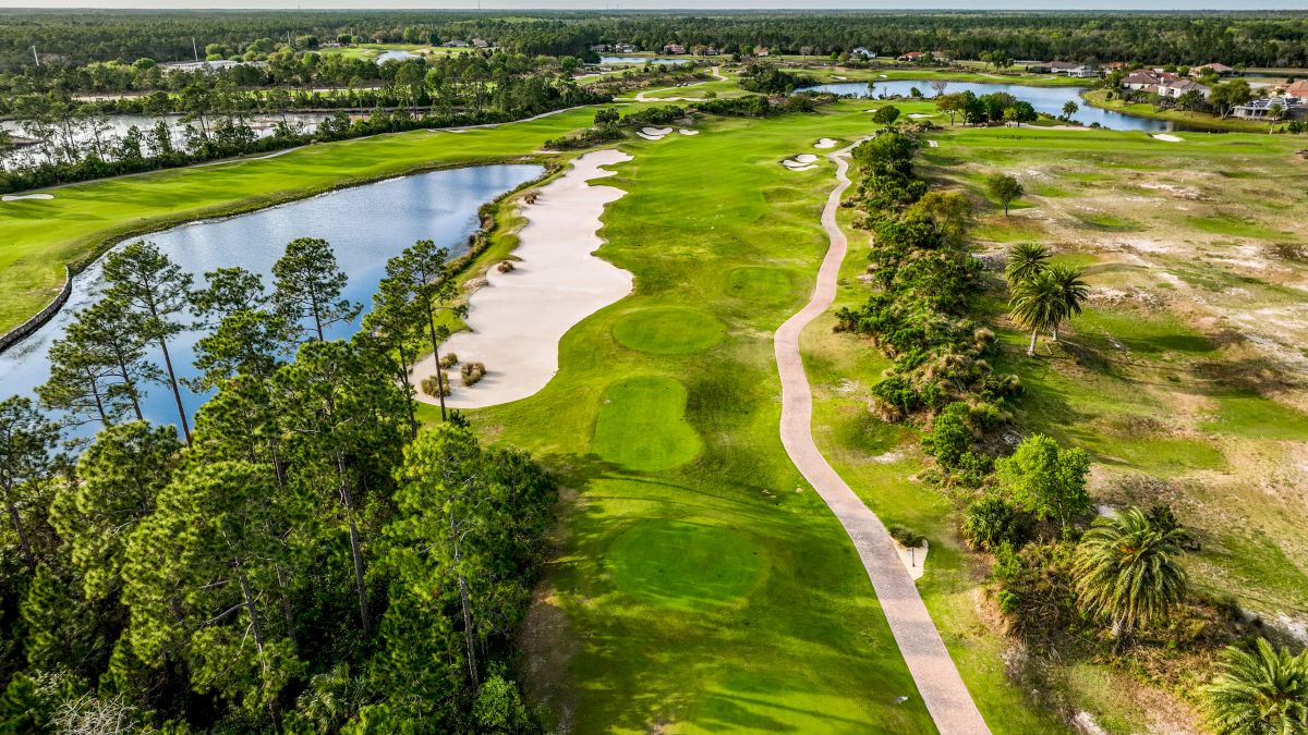 An aerial view of a golf course features a fairway, sand traps, a pond, and a path lined with trees.