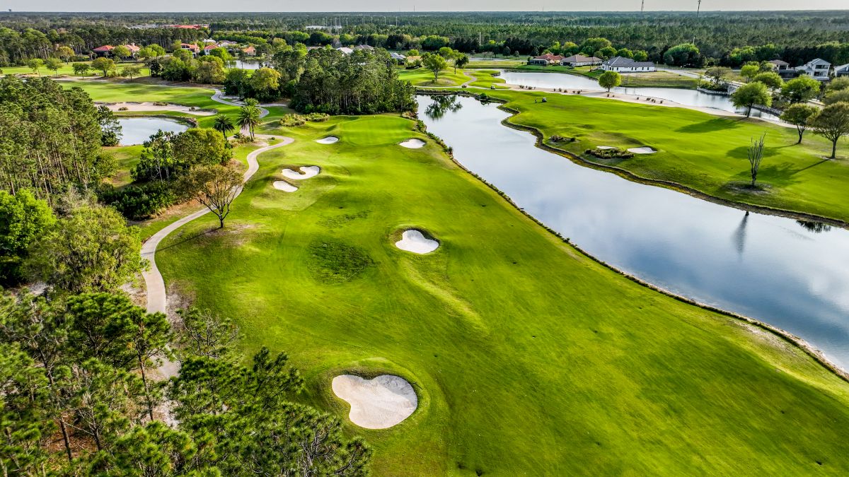 An aerial view of a lush golf course with sand traps and a winding river.