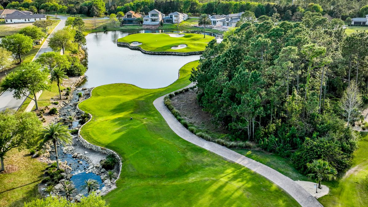 Aerial view of a golf course featuring manicured greens, a winding path, a small lake, and surrounding trees intersecting with residential homes.