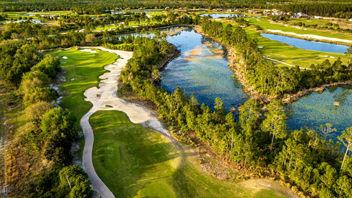 Aerial view of a golf course with lush greens, sand bunkers, and surrounding water features and vegetation in a vast landscape.