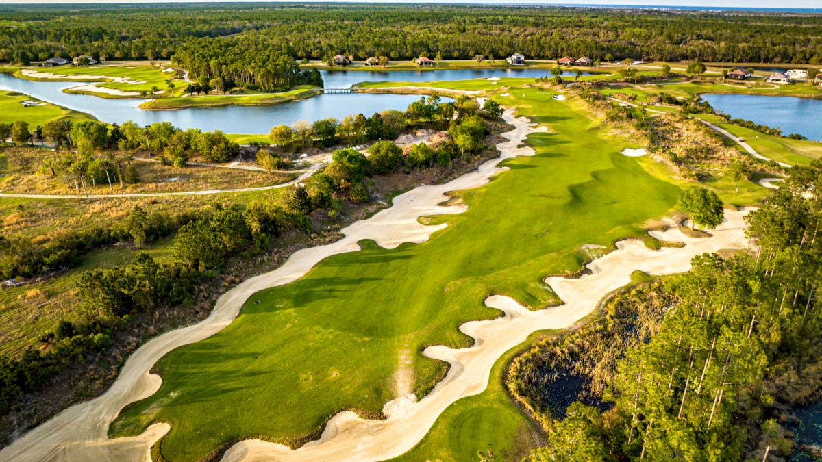 Aerial view of a golf course with sand traps, green fairways, lakes, and surrounding trees.