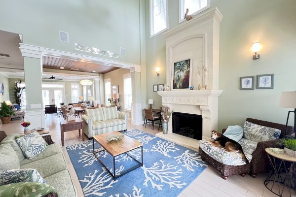 A spacious living room with high ceilings, comfy furniture, a fireplace, and large windows. A dog relaxes on a chair.