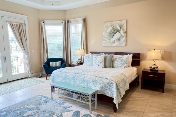 A spacious bedroom with a large bed, two bedside tables with lamps, and a sitting area by windows with curtains and patterned decor.