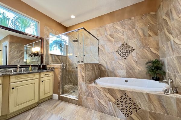 A modern bathroom featuring a glass shower, a bathtub with decorative tiles, and a counter with a sink and mirror.