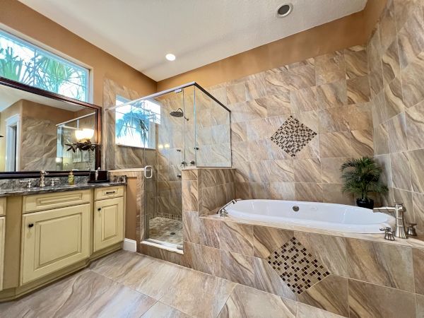 A modern bathroom featuring a glass shower, a bathtub with decorative tiles, and a counter with a sink and mirror.