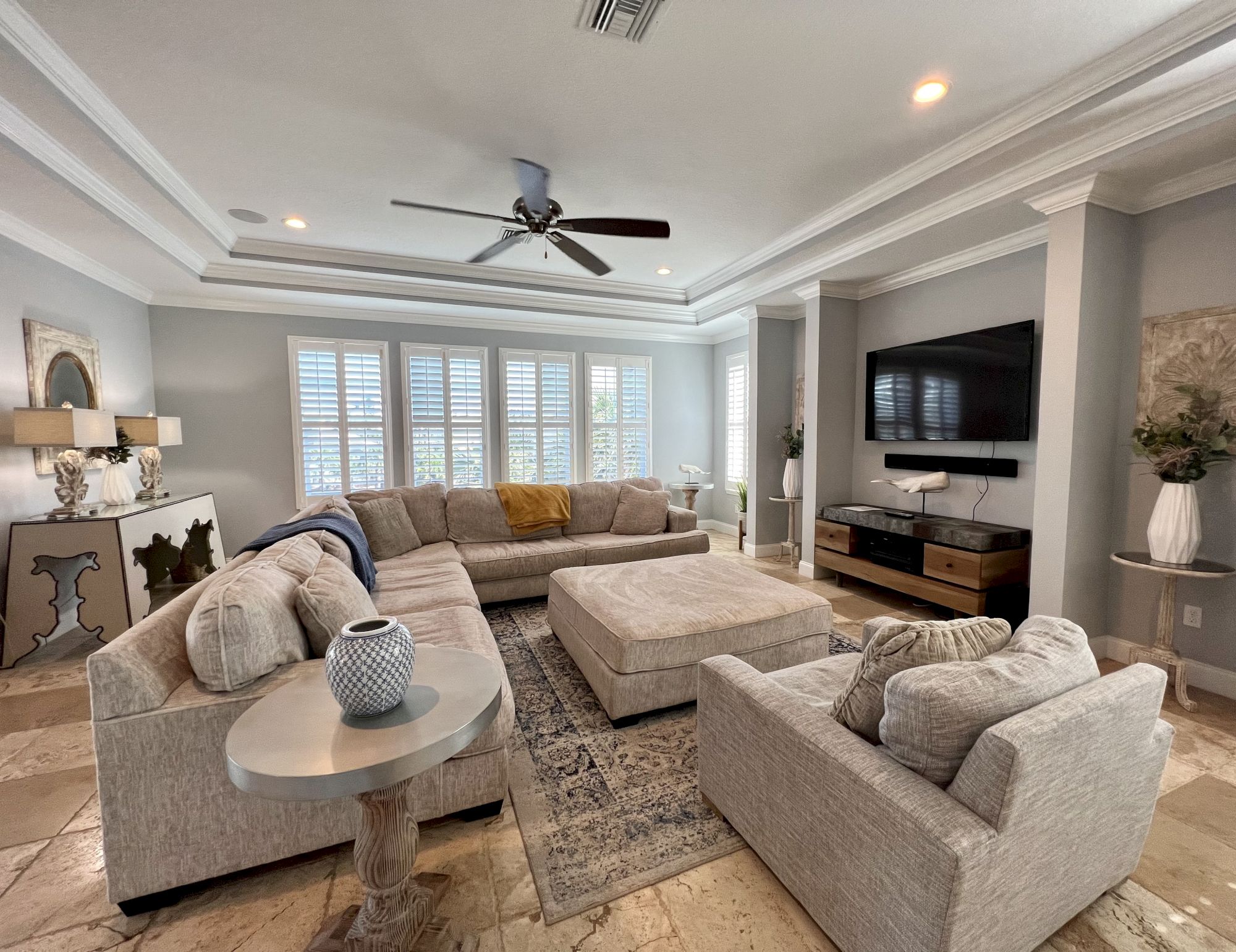 A cozy living room with a large sectional sofa, TV, and elegant decor. Natural light filters through the windows, creating a serene space.
