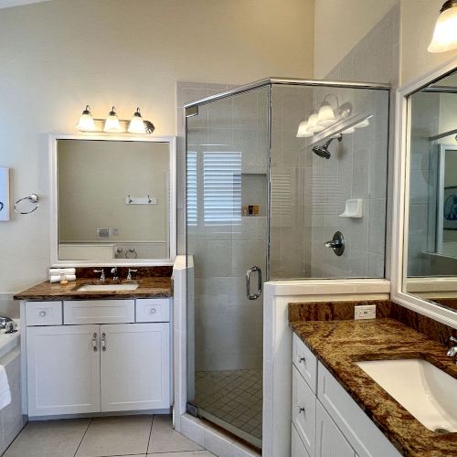 A modern bathroom with a shower, double sinks, a tub, and artwork on the wall. Bright lighting and neutral tones decorate the space.
