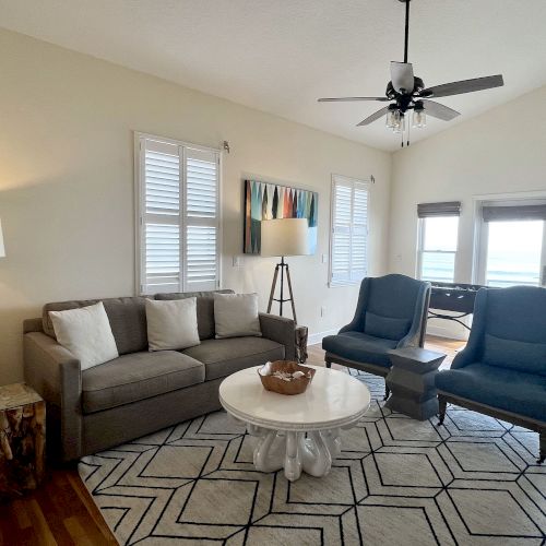A modern living room with a gray sofa, two blue armchairs, a round white coffee table, floor lamps, and a geometric rug.