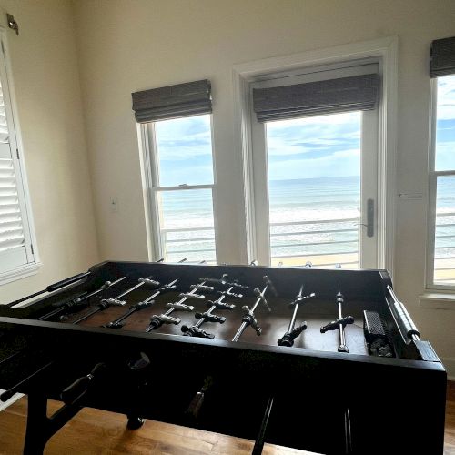 A foosball table is in a room with two windows and an ocean view.