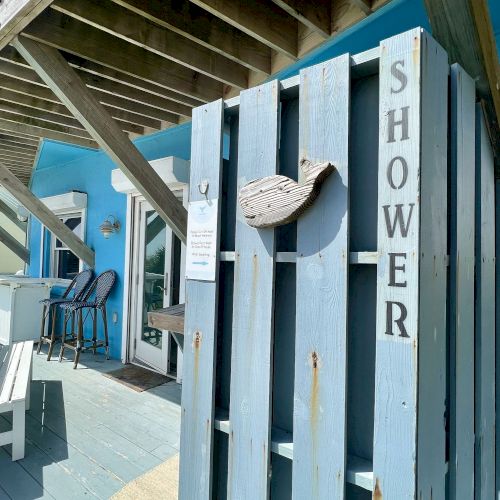 An outdoor shower with a rustic design is set against a blue wall, featuring a wooden structure and beach-themed decor.