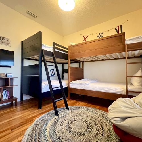 The image shows a room with two bunk beds, a round rug, a bean bag chair, a bookshelf, and a wall-mounted TV.