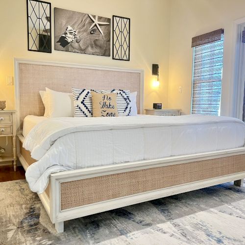 A cozy bedroom with a white bed, patterned pillows, nightstands, wall art, and a rug, conveying a warm and inviting atmosphere.