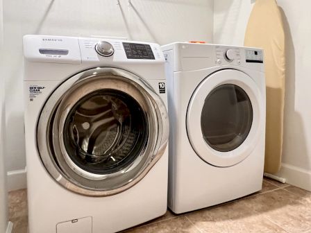 A laundry room with a front-load washing machine, a front-load dryer, and an ironing board against the wall.
