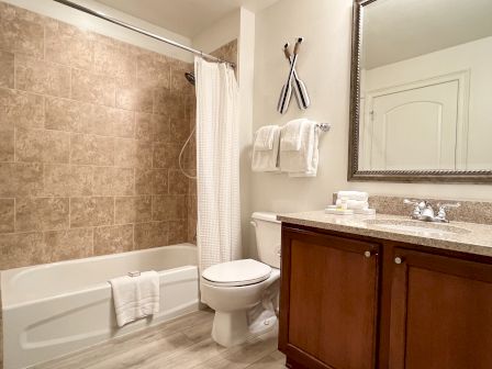 A clean bathroom with a tub and shower, toilet, towels, large mirror, wooden cabinet, and decorative oars above the towels.