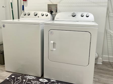 A white washing machine and dryer are side by side on a floral mat in a laundry room.