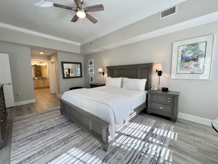 A modern bedroom with a bed, nightstands, and a ceiling fan. Light wood flooring, wall art, and neutral colors create a calm, stylish space.