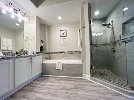 A modern bathroom with a glass shower, corner bathtub, large vanity, and decorative wall art, featuring soft lighting.
