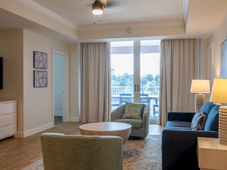 Bright modern living room with sofas, a round coffee table, curtains, and a large window/door to a balcony.