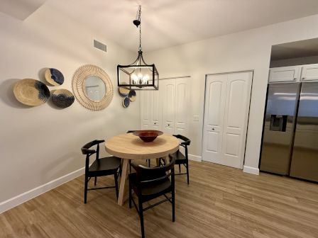 A dining area with a round wooden table, black chairs, a red bowl, decorative wall baskets, a mirror, and a modern chandelier.