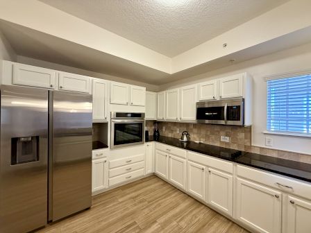 A modern kitchen with white cabinets, stainless steel appliances, tiled backsplash, and wooden floors, featuring a double door fridge.