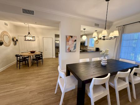 A modern dining area with two tables, chairs, wall art, decorative mirrors, and stylish lighting. The setting appears organized and inviting.