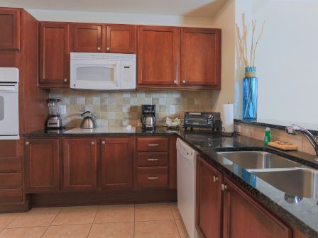 A kitchen with wooden cabinets, a microwave, oven, blender, kettle, coffee maker, toaster, and double sink on a granite countertop.