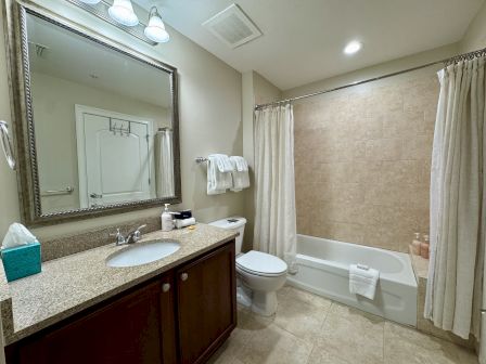 A clean bathroom features a vanity with a large mirror, sink, towels, bathtub with curtain, and tiled walls and floor.