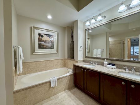 A bathroom with a large mirror, dual sinks, a framed picture, and a bathtub with towels on it.