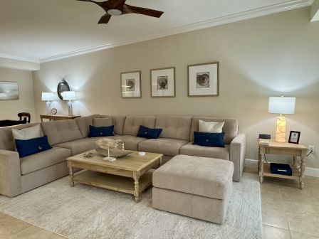 A cozy living room features a beige sectional sofa with navy cushions, wooden coffee table, modern lamps, and framed artwork on the wall.