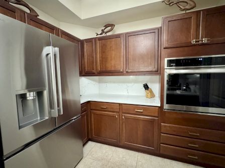 A kitchen with wooden cabinets, a large stainless steel refrigerator, an oven, countertop, and a knife block with knives.